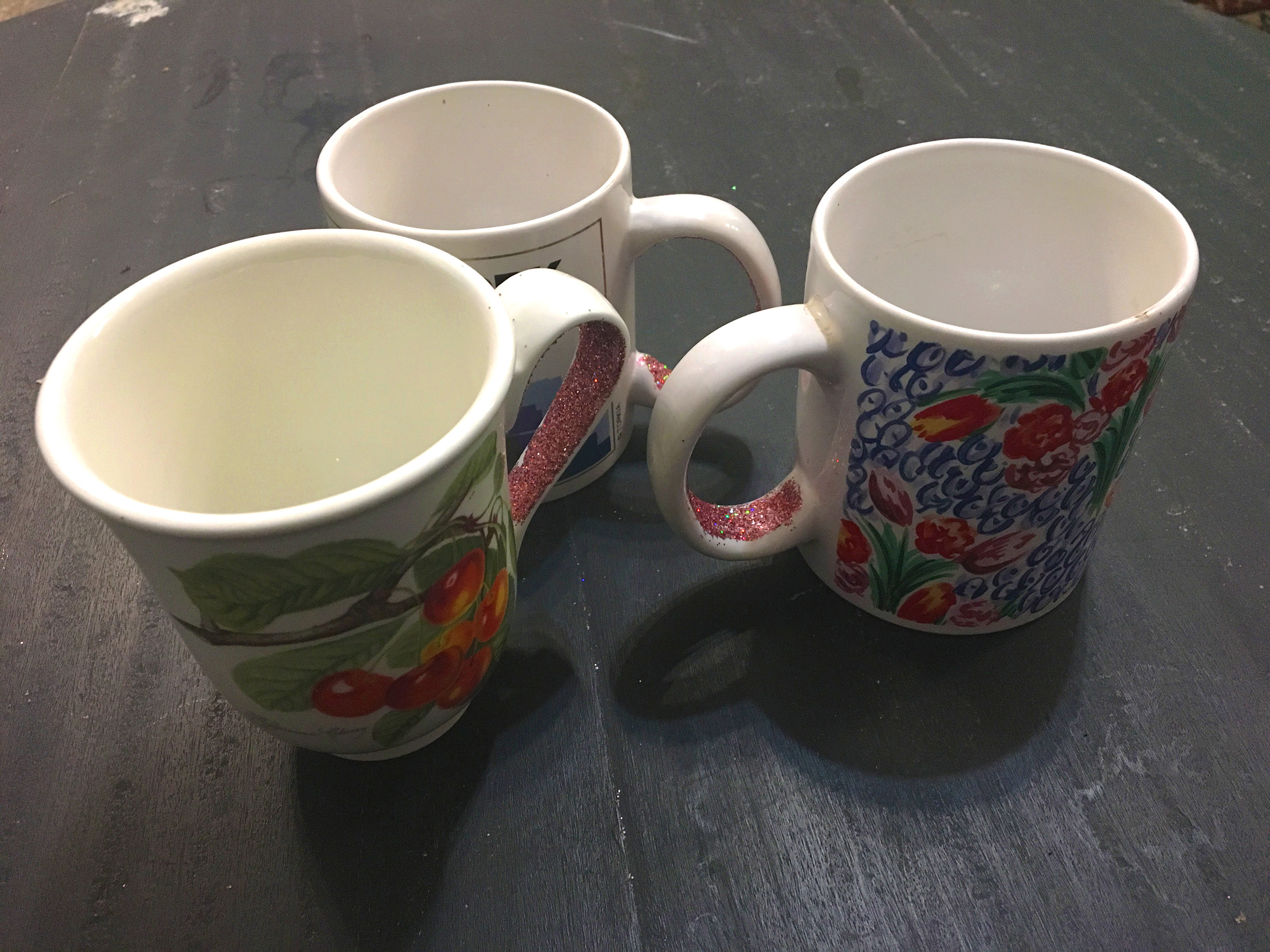 Trois mugs sont posés sur une table. On voit que des paillettes sont collées à l'intérieur des hanses.